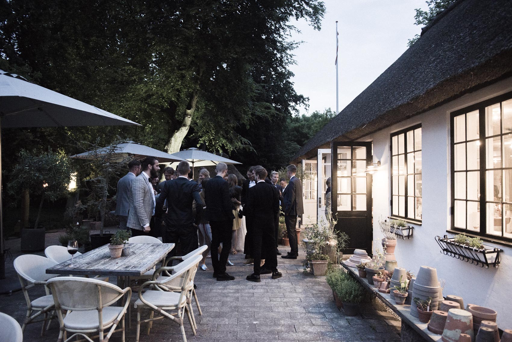 Gæsterne på terrassen ved Restaurant Herthadalen i aftenlys, omgivet af smuk grøn natur under Kathrine og Michaels bryllupsfest, fotograferet af To the Moon and Back.